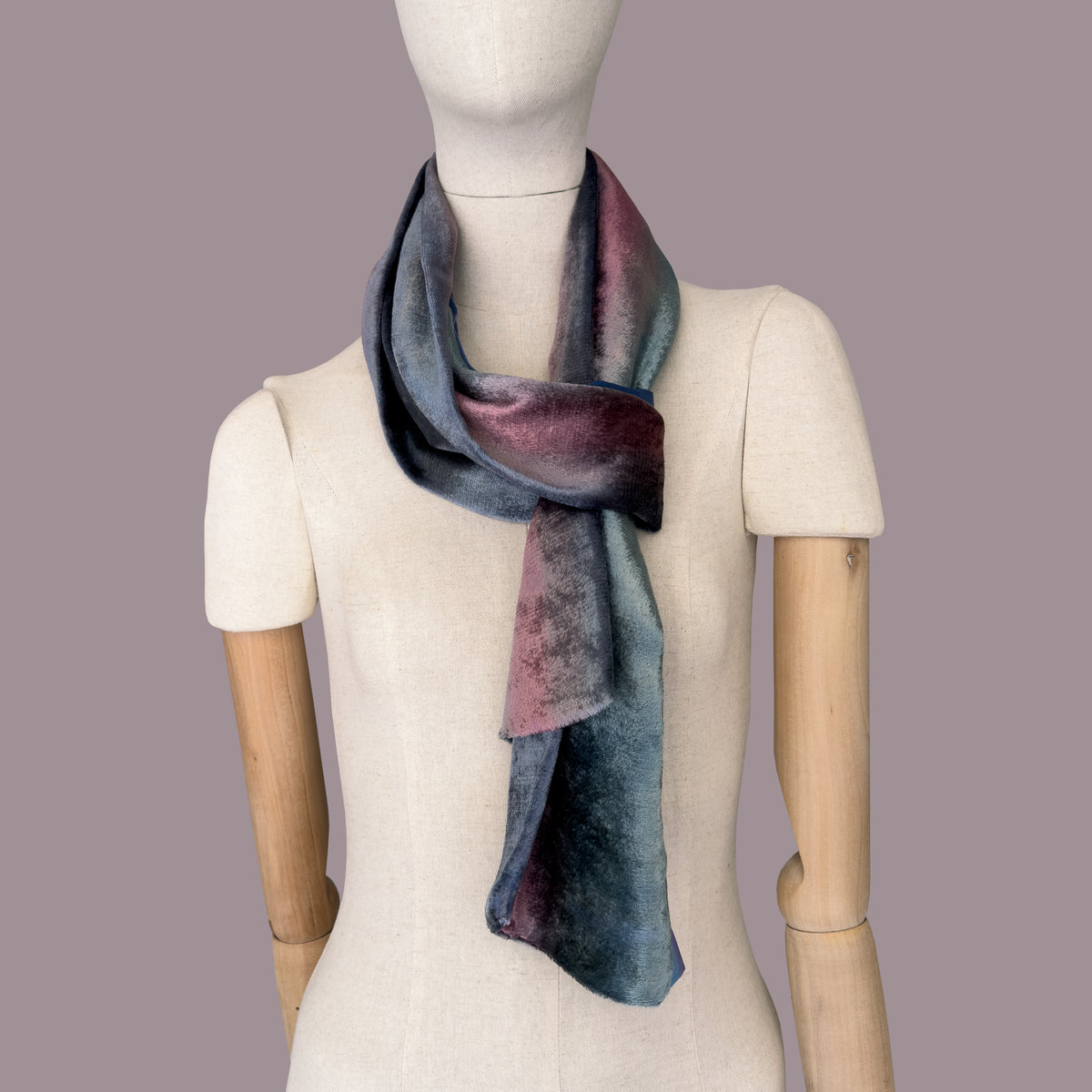 Mannequin wearing a colorful velvet scarf on a gray background. Velvet scarf is in shades of green, pink and blue navy colors. It is hand-painted scarf in measures 180 x 20 cm by otta-italy scarves brand.