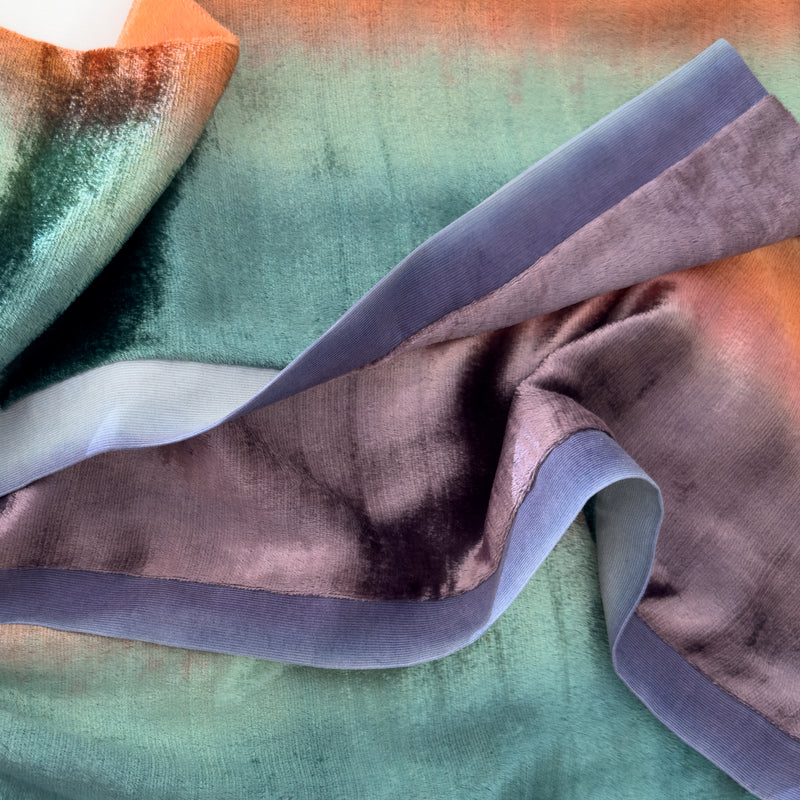 Close-up of a hand-painted Otta-Italy velvet scarf showcasing the tactile contrast between the plush emerald green and brick red velvet body and the smooth blue and purple hand-sewn cotton border.
