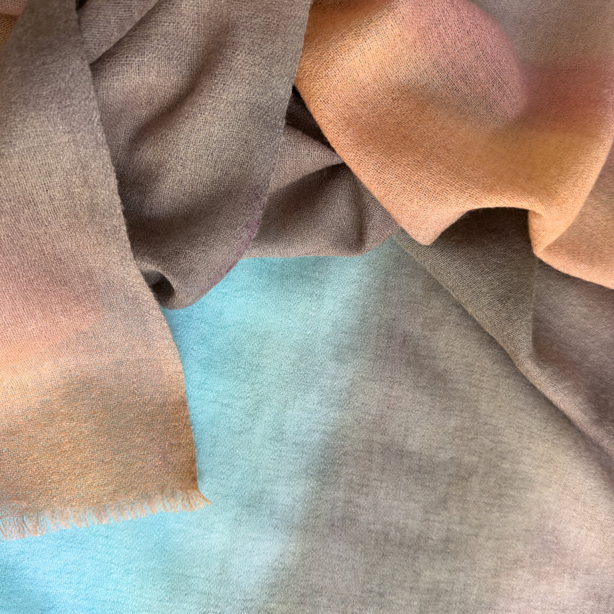 Close-up of soft fabric. Hand-painted wool scarf by Otta-Italy, 56 x 177 cm, featuring brown, turquoise, peach colors. Luxury Italian mix accessory, soft and warm scarf for women and men.
