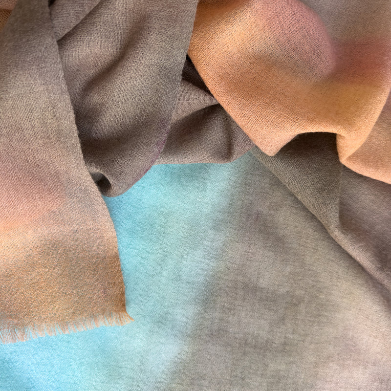 Close-up of a hand-painted Otta-Italy pure wool scarf showcasing rich shades of brown, turquoise, and peach with delicate hand-fringed edges.