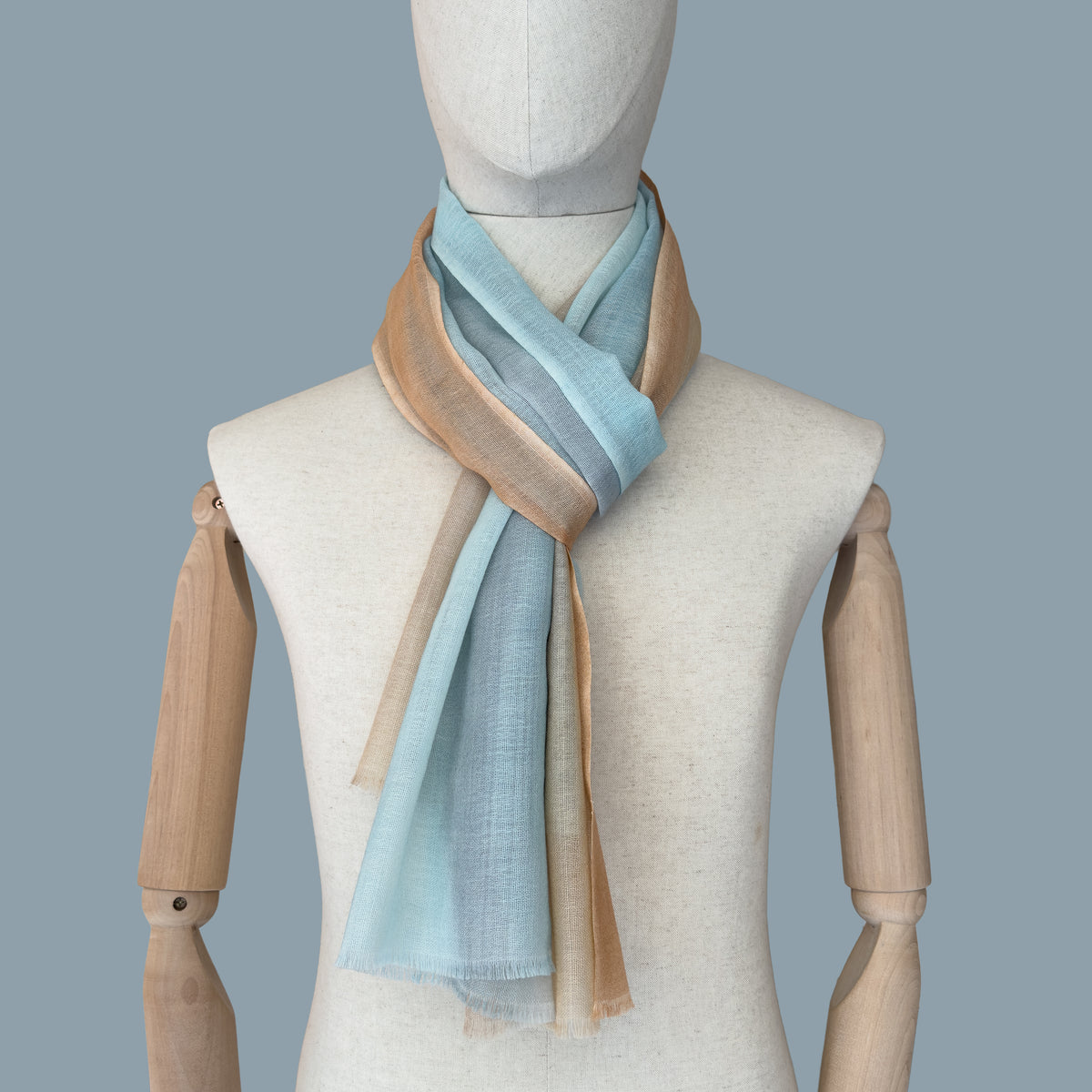 Mannequin wearing scarf on a gray background. Hand-painted wool scarf by Otta-Italy, 61 x 197 cm, featuring 
blue, gray and ocher. Luxury Italian pure wool accessory, soft and warm scarf for women and men.
