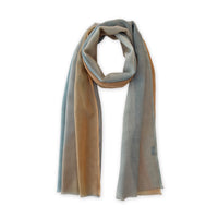 Hand-painted Otta wool scarf in 
blue, gray and ocher, loosely looped to showcase its full length and delicate texture in white background. Lightweight artisan accessory with hand-fringed edges, measuring 61 x 197 cm.
