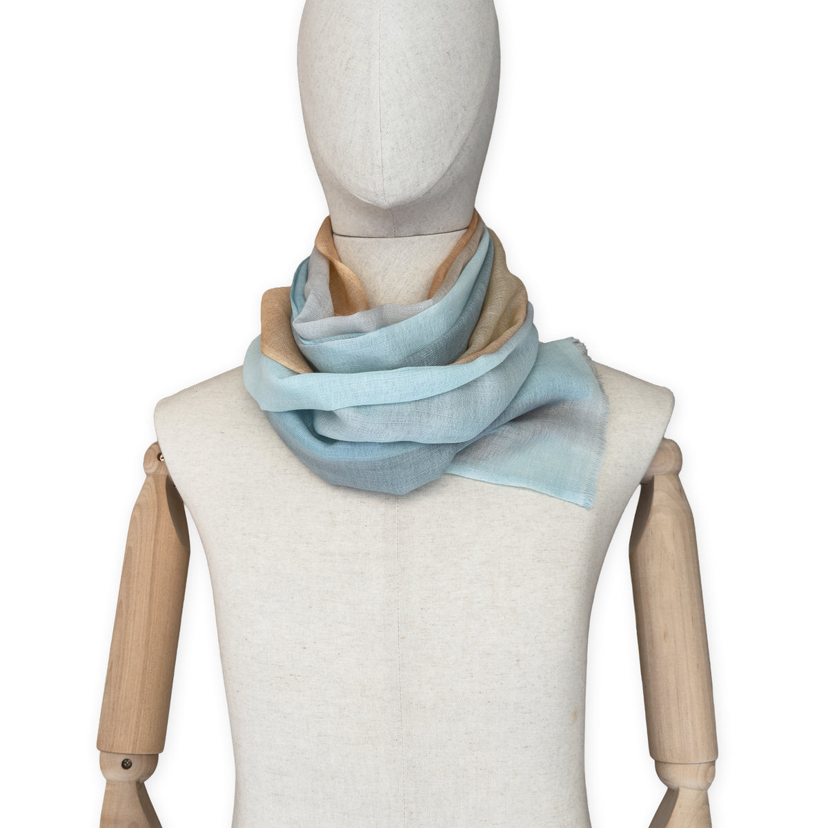 Mannequin wearing a hand-painted Otta wool scarf on a white background in 
blue, gray and ocher tones. Lightweight, warm, and elegant accessory measuring 61 x 197 cm. Unique artisan scarf with hand-fringed edges, perfect for women and men.
