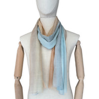 Mannequin wearing a hand-painted Otta wool scarf on a white background in 
blue, gray and ocher tones. Lightweight, warm, and elegant accessory measuring 61 x 197 cm. Unique artisan scarf with hand-fringed edges, perfect for women and men.
