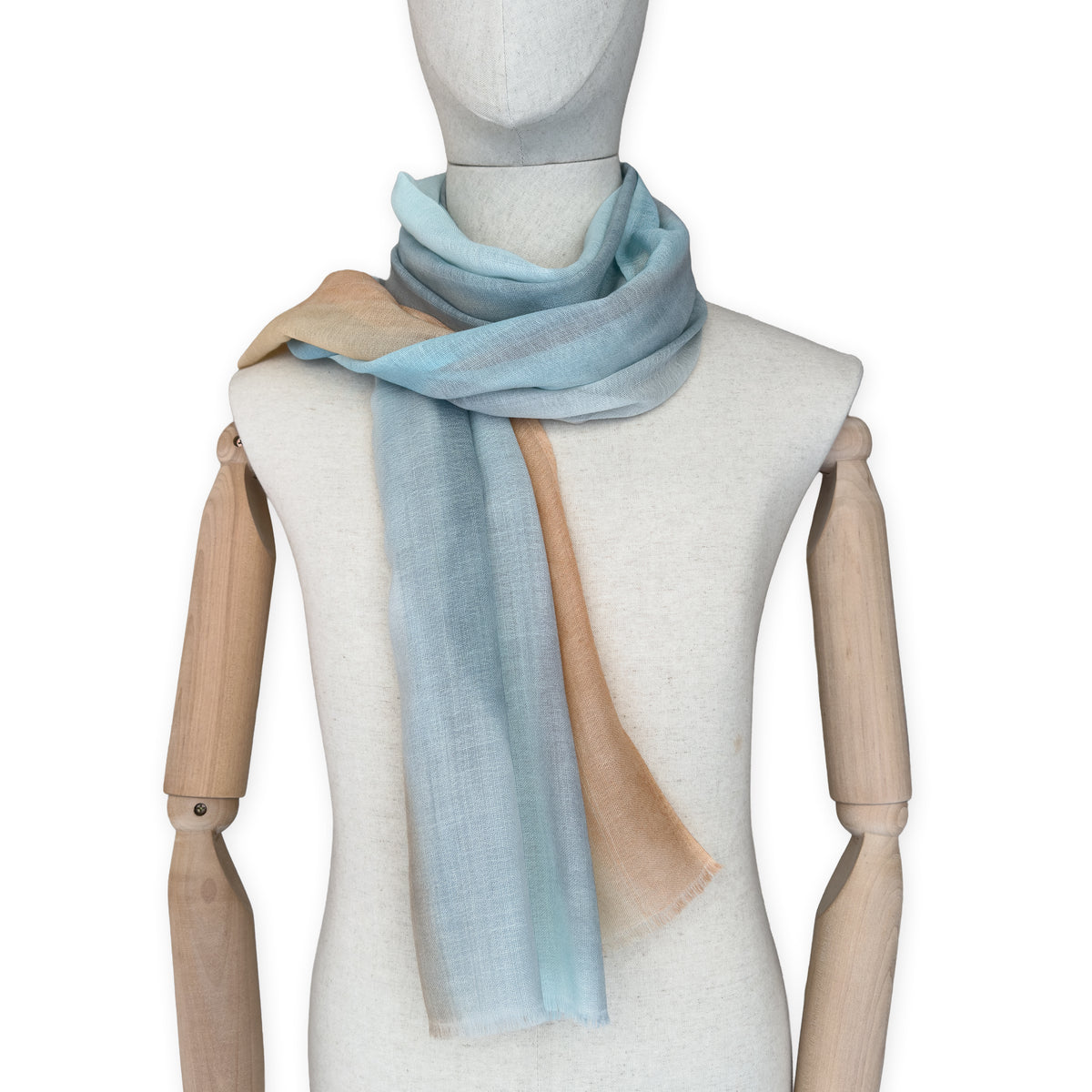 Mannequin wearing a hand-painted Otta wool scarf on a white background in 
blue, gray and ocher tones. Lightweight, warm, and elegant accessory measuring 61 x 197 cm. Unique artisan scarf with hand-fringed edges, perfect for women and men.
