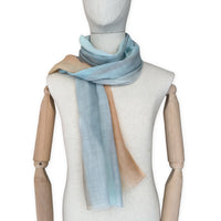Mannequin wearing a hand-painted Otta wool scarf on a white background in 
blue, gray and ocher tones. Lightweight, warm, and elegant accessory measuring 61 x 197 cm. Unique artisan scarf with hand-fringed edges, perfect for women and men.
