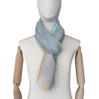 Mannequin wearing a hand-painted Otta wool scarf on a white background in 
blue, gray and ocher tones. Lightweight, warm, and elegant accessory measuring 61 x 197 cm. Unique artisan scarf with hand-fringed edges, perfect for women and men.

