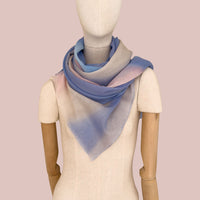 Mannequin wearing a hand-painted pure wool scarf by Otta-Italy, pink background. Blue, pink, beige and gray shades. 62 x 203 cm.
