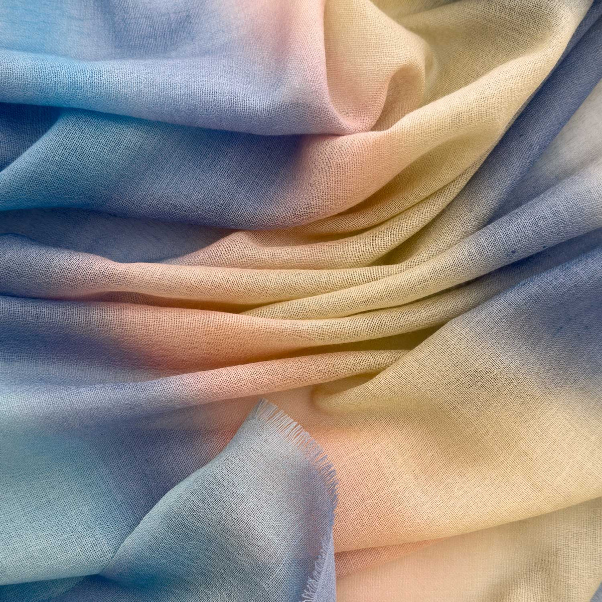 Close-up of hand-painted Otta pure wool scarf showcasing soft blue, pink, beige and gray shades with delicate hand-fringed edges.
