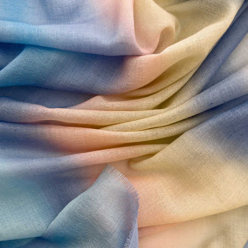 Close-up of hand-painted Otta pure wool scarf showcasing soft blue, pink, beige and gray shades with delicate hand-fringed edges.

