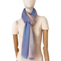 Mannequin wearing an elegant hand-painted Otta pure wool scarf on a white background. Warm blue, pink, beige and gray tones.
