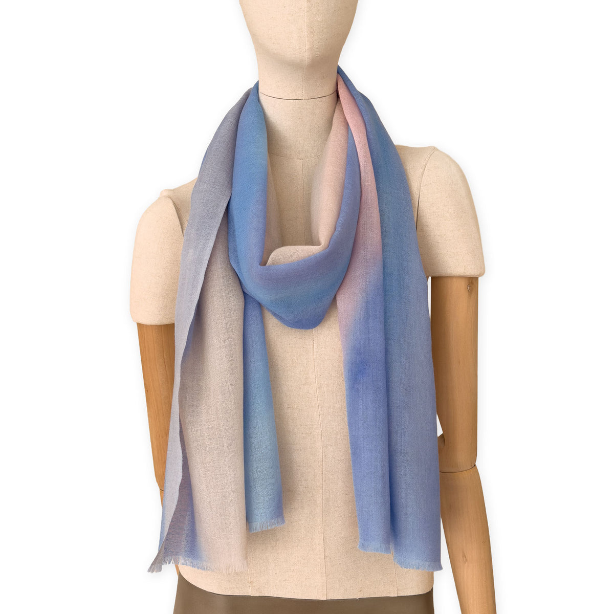 Mannequin wearing an elegant hand-painted Otta pure wool scarf on a white background. Warm blue, pink, beige and gray tones.
