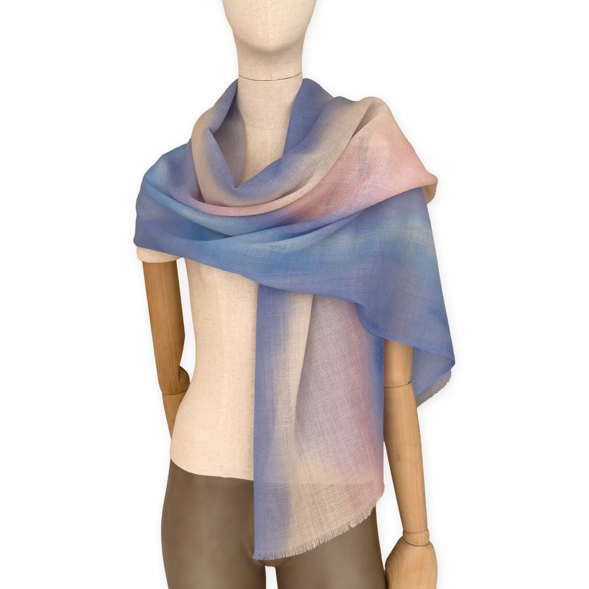 Mannequin wearing an elegant hand-painted Otta pure wool scarf on a white background. Warm blue, pink, beige and gray tones.

