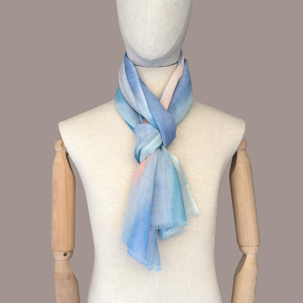 Mannequin wearing scarf on a beige background. Hand-painted wool scarf by Otta-Italy, 61 x 197 cm, featuring 
pastel blue and pink. Luxury Italian pure wool accessory, soft and warm scarf for women and men.
