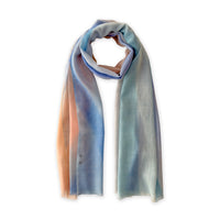 Hand-painted Otta wool scarf in 
pastel blue and pink, loosely looped to showcase its full length and delicate texture in white background. Lightweight artisan accessory with hand-fringed edges, measuring 61 x 197 cm.
