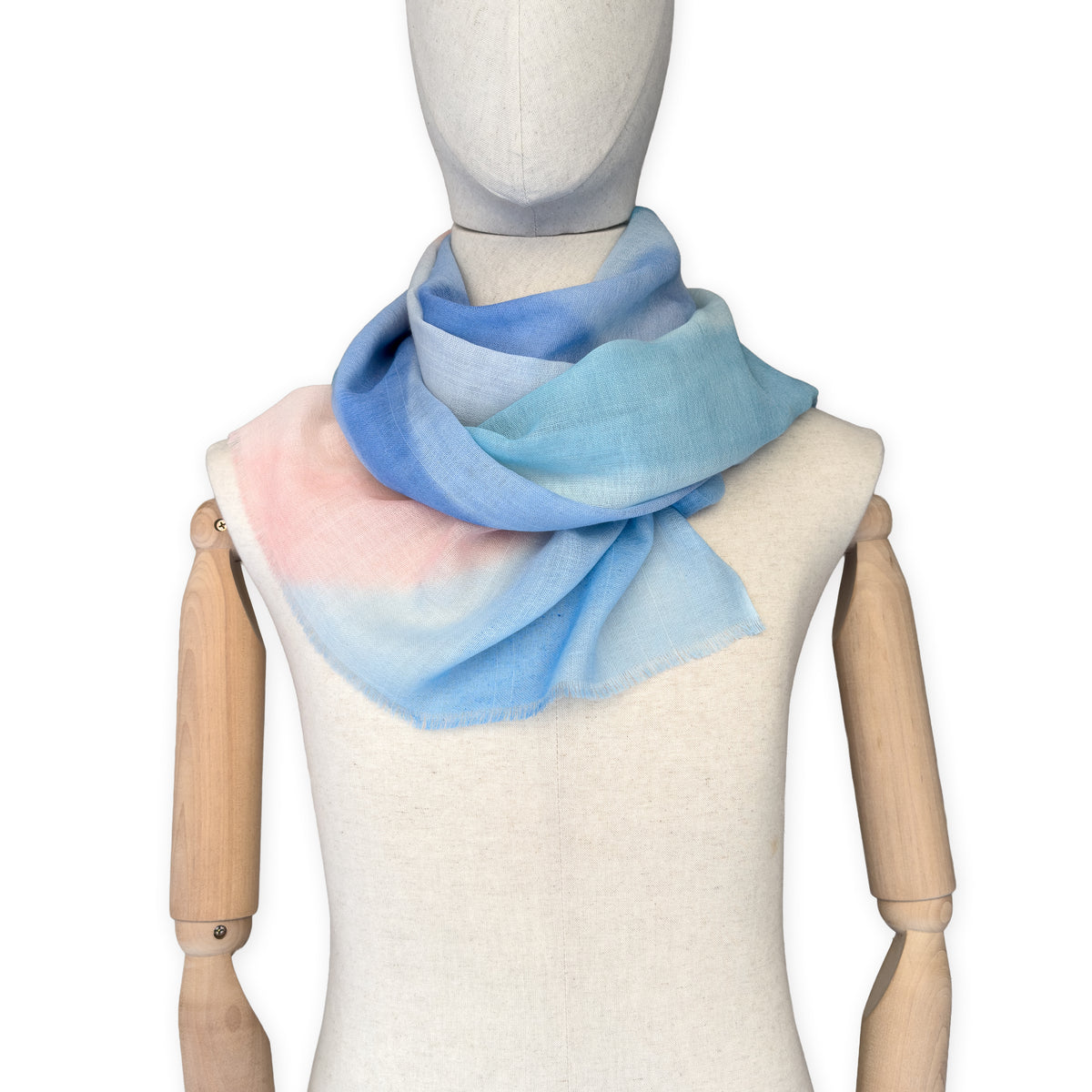Mannequin wearing a hand-painted Otta wool scarf on a white background in 
pastel blue and pink tones. Lightweight, warm, and elegant accessory measuring 61 x 197 cm. Unique artisan scarf with hand-fringed edges, perfect for women and men.
