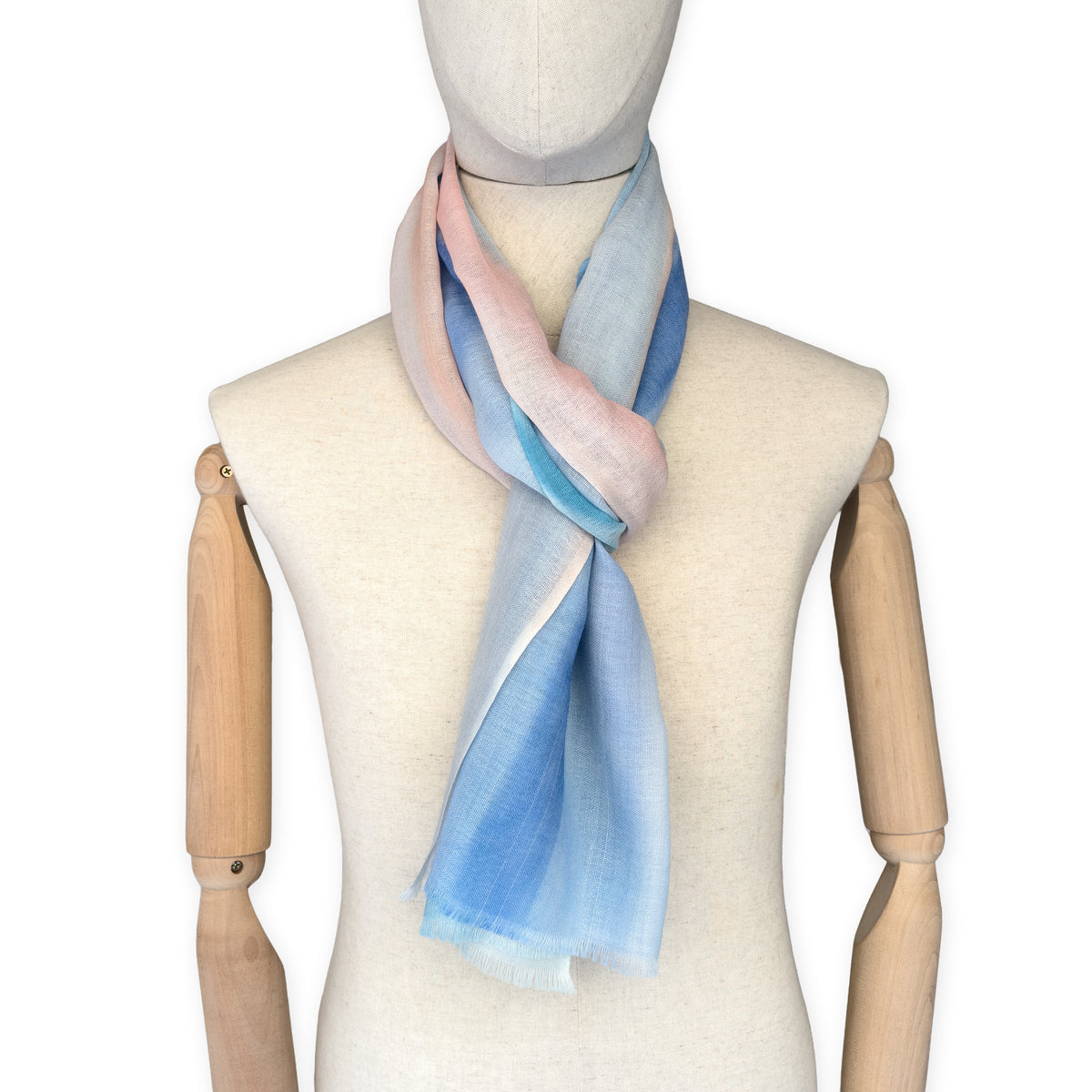 Mannequin wearing a hand-painted Otta wool scarf on a white background in 
pastel blue and pink tones. Lightweight, warm, and elegant accessory measuring 61 x 197 cm. Unique artisan scarf with hand-fringed edges, perfect for women and men.
