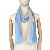 Mannequin wearing a hand-painted Otta wool scarf on a white background in 
pastel blue and pink tones. Lightweight, warm, and elegant accessory measuring 61 x 197 cm. Unique artisan scarf with hand-fringed edges, perfect for women and men.
