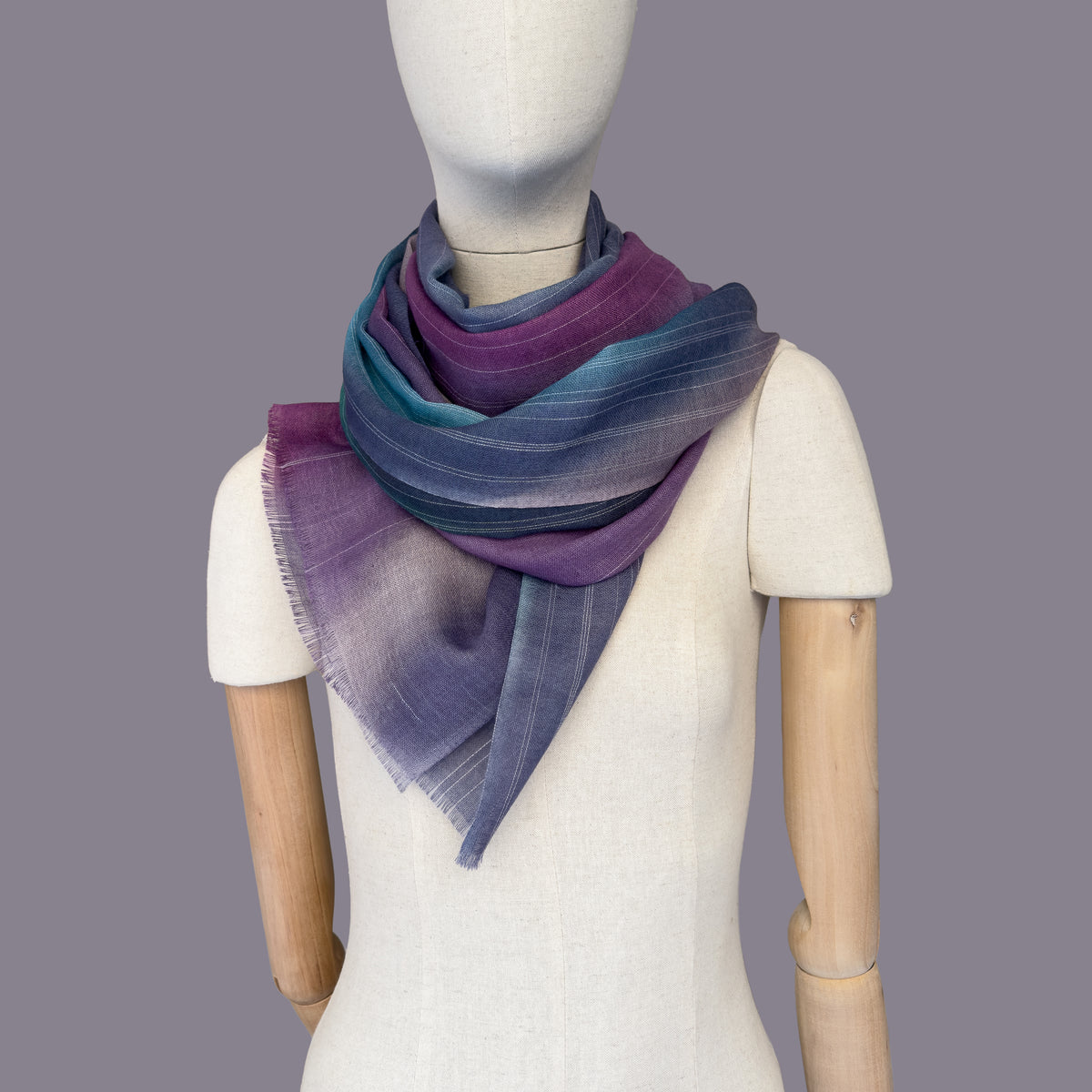 Mannequin wearing scarf on a gray background. Hand-painted wool scarf by Otta-Italy, 61 x 197 cm, featuring 
purple, emerald green and light blue. Luxury Italian pure wool accessory, soft and warm scarf for women and men.
