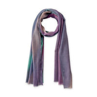 Hand-painted Otta wool scarf in 
purple, emerald green and light blue, loosely looped to showcase its full length and delicate texture in white background. Lightweight artisan accessory with hand-fringed edges, measuring 61 x 197 cm.
