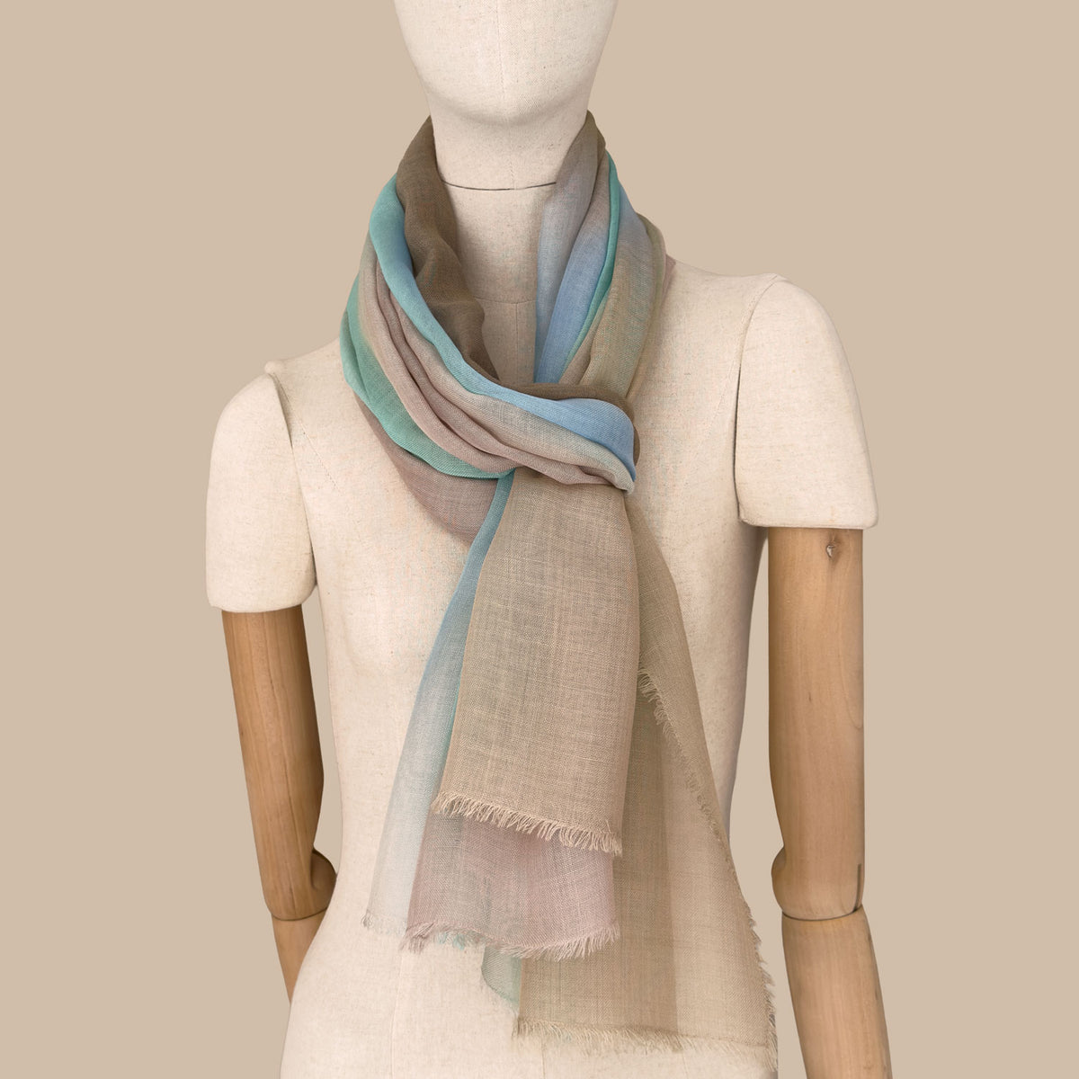 Mannequin wearing a hand-painted wool silk blend scarf by Otta-Italy, beige background. Brown, beige, light blue and turquoise shades. 69 x 198 cm.
