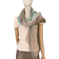 Mannequin wearing an elegant hand-painted Otta wool silk blend scarf on a white background. Warm brown, beige, light blue and turquoise tones.
