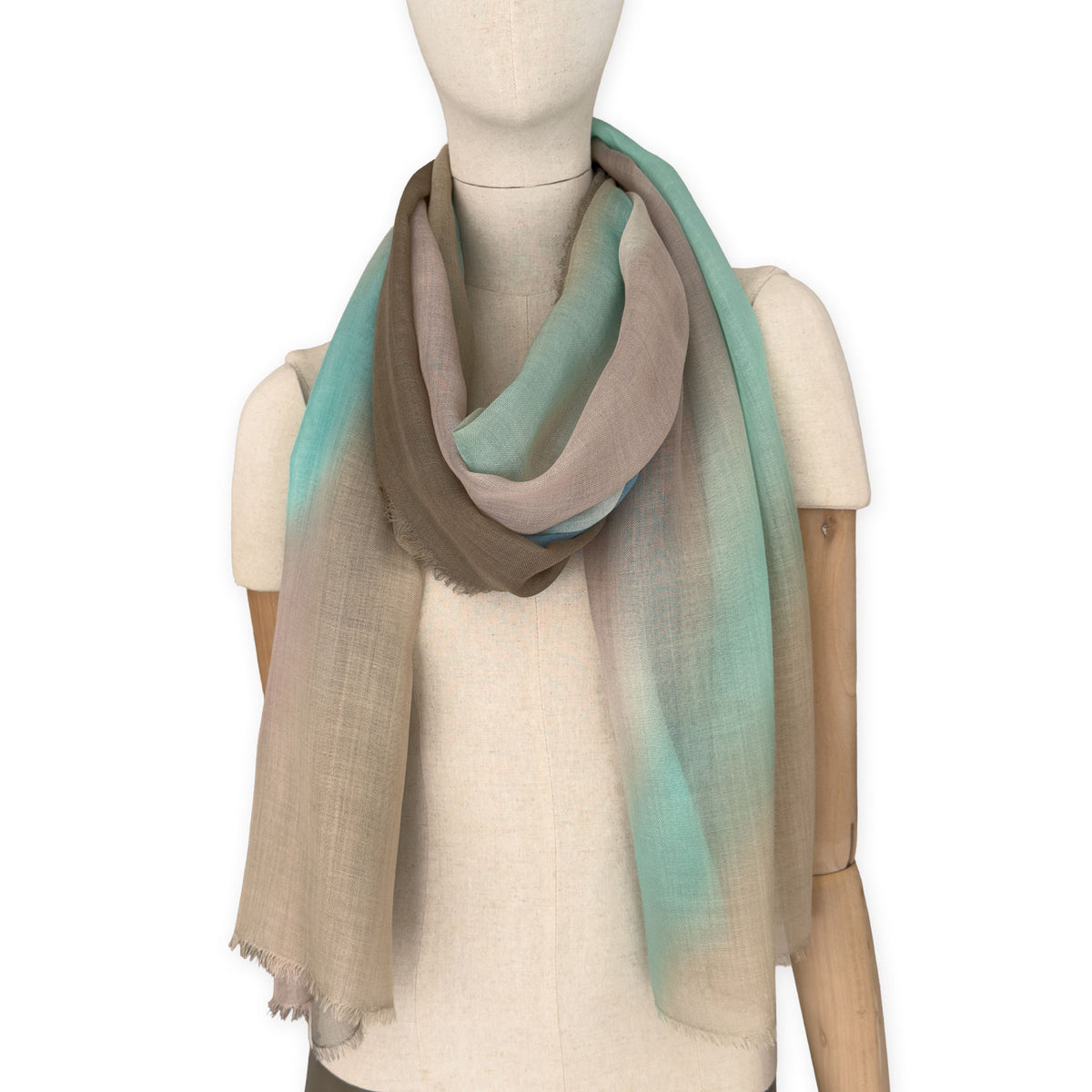 Mannequin wearing an elegant hand-painted Otta wool silk blend scarf on a white background. Warm brown, beige, light blue and turquoise tones.
