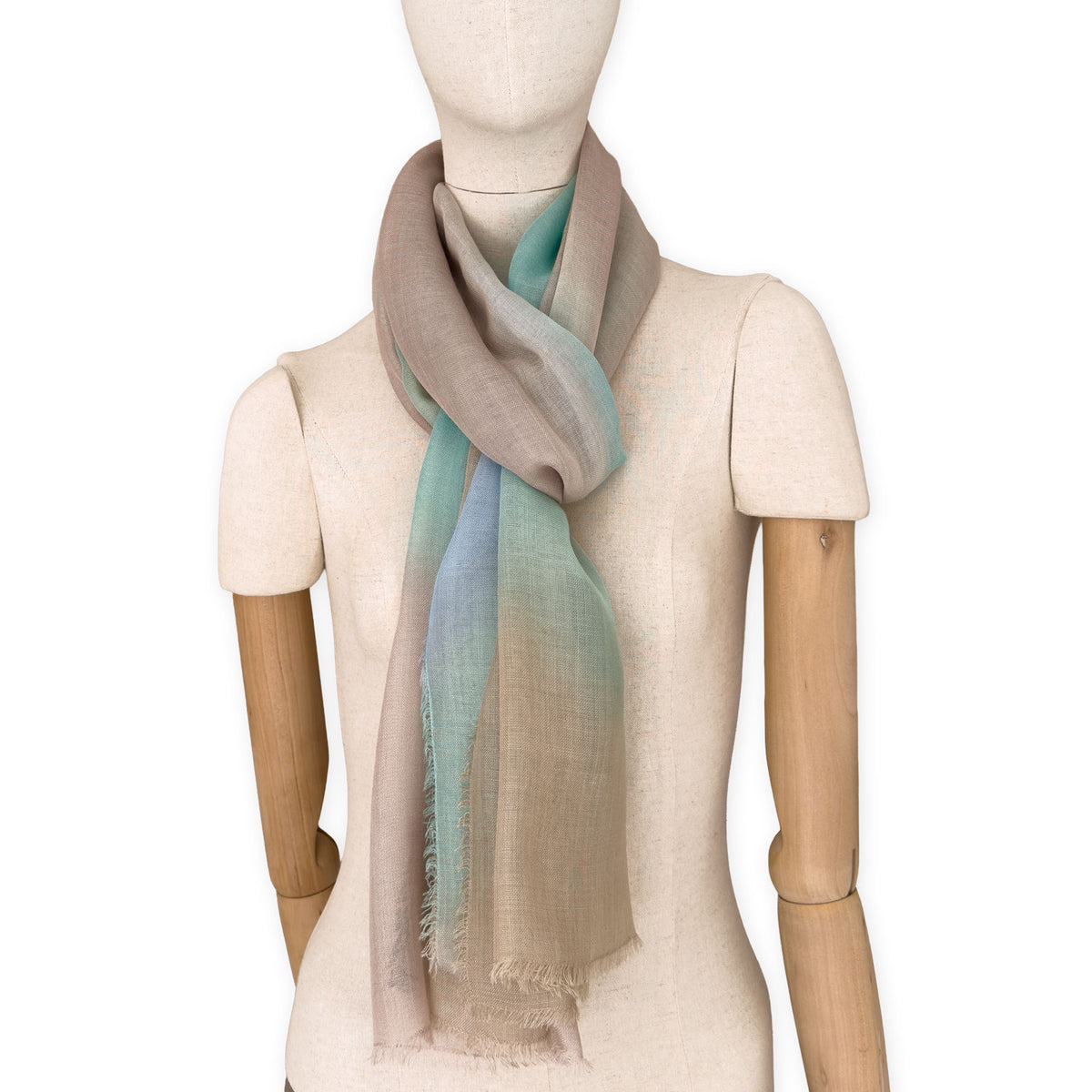 Mannequin wearing an elegant hand-painted Otta wool silk blend scarf on a white background. Warm brown, beige, light blue and turquoise tones.
