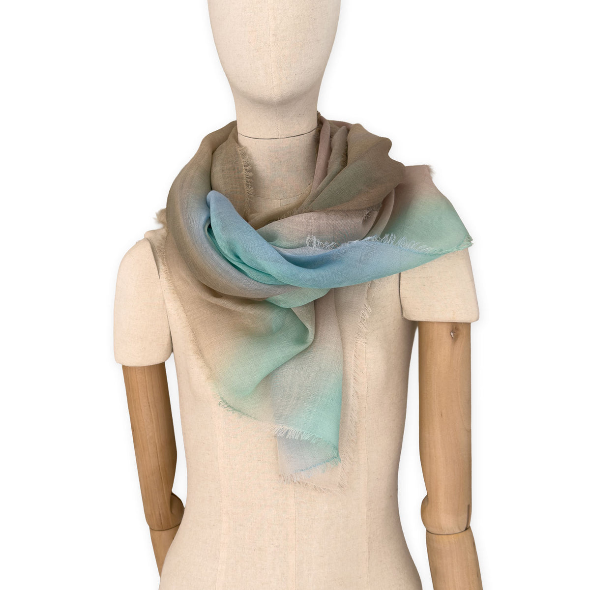 Mannequin wearing an elegant hand-painted Otta wool silk blend scarf on a white background. Warm brown, beige, light blue and turquoise tones.
