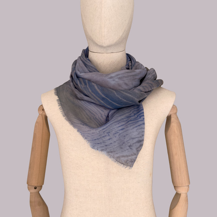 Mannequin wearing a hand-painted wool silk blend scarf by Otta-Italy, gray background. Blue, gray and brown. 68x194 cm.
