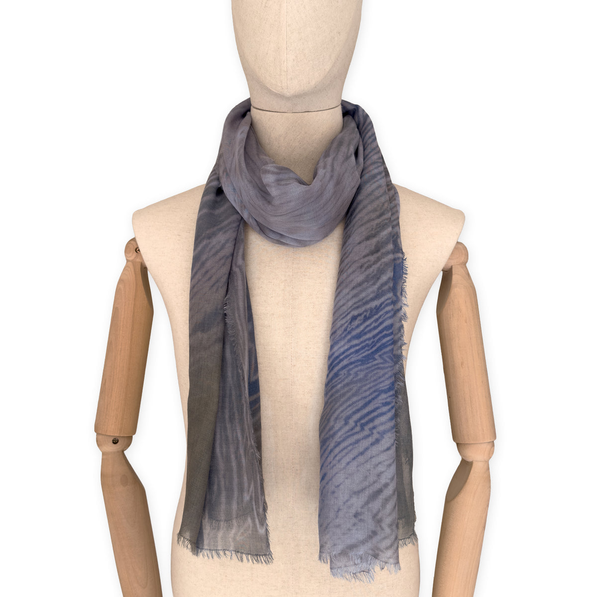 Mannequin wearing an elegant hand-painted Otta wool silk blend scarf on a white background. Blue, gray and brown tones.
