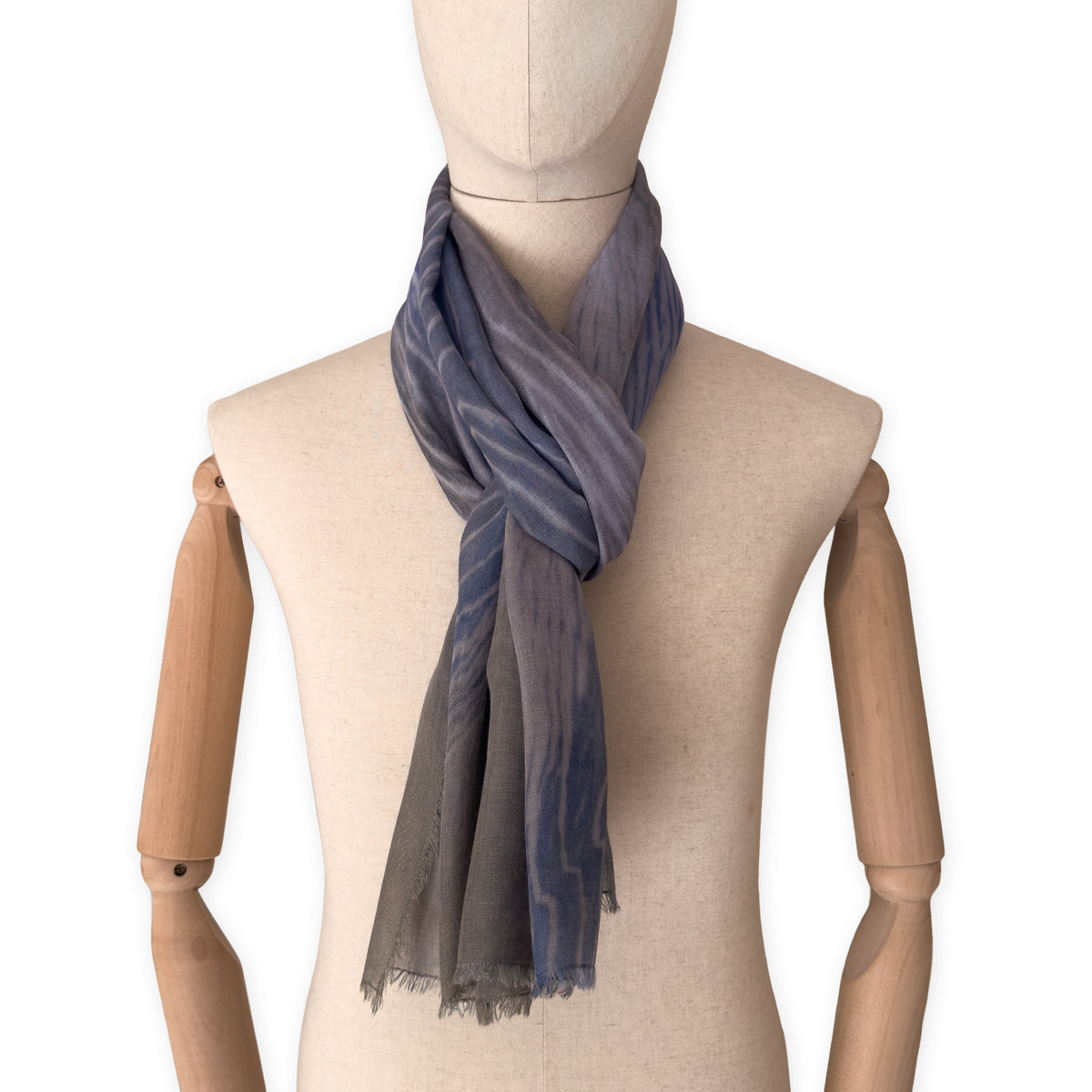 Mannequin wearing an elegant hand-painted Otta wool silk blend scarf on a white background. Blue, gray and brown tones.
