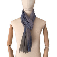 Mannequin wearing an elegant hand-painted Otta wool silk blend scarf on a white background. Blue, gray and brown tones.

