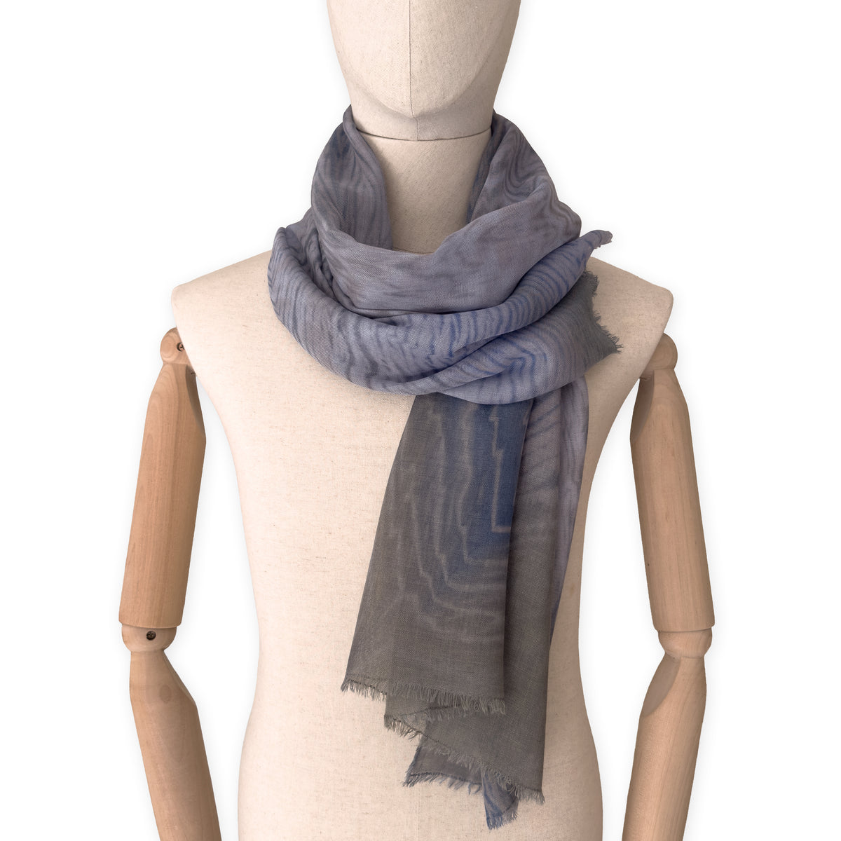 Mannequin wearing an elegant hand-painted Otta wool silk blend scarf on a white background. Blue, gray and brown tones.
