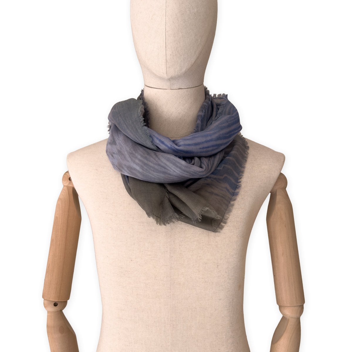 Mannequin wearing an elegant hand-painted Otta wool silk blend scarf on a white background. Blue, gray and brown tones.
