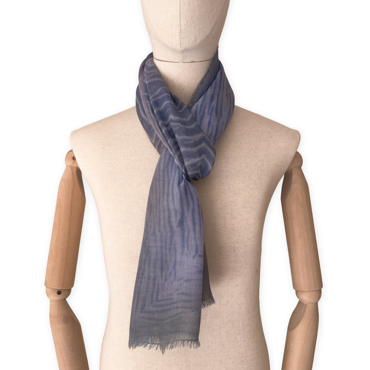 Mannequin wearing an elegant hand-painted Otta wool silk blend scarf on a white background. Blue, gray and brown tones.
