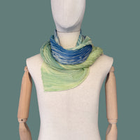 Mannequin wearing scarf on a green background. Hand-painted wool & silk scarf by Otta-Italy, 54 x 193 cm, featuring 
blue, light green and yellow. Luxury Italian wool & silk accessory, soft and warm scarf for women and men.
