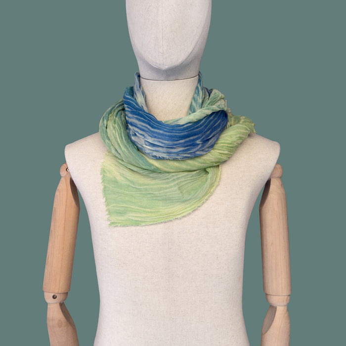 Mannequin wearing scarf on a green background. Hand-painted wool & silk scarf by Otta-Italy, 54 x 193 cm, featuring 
blue, light green and yellow. Luxury Italian wool & silk accessory, soft and warm scarf for women and men.
