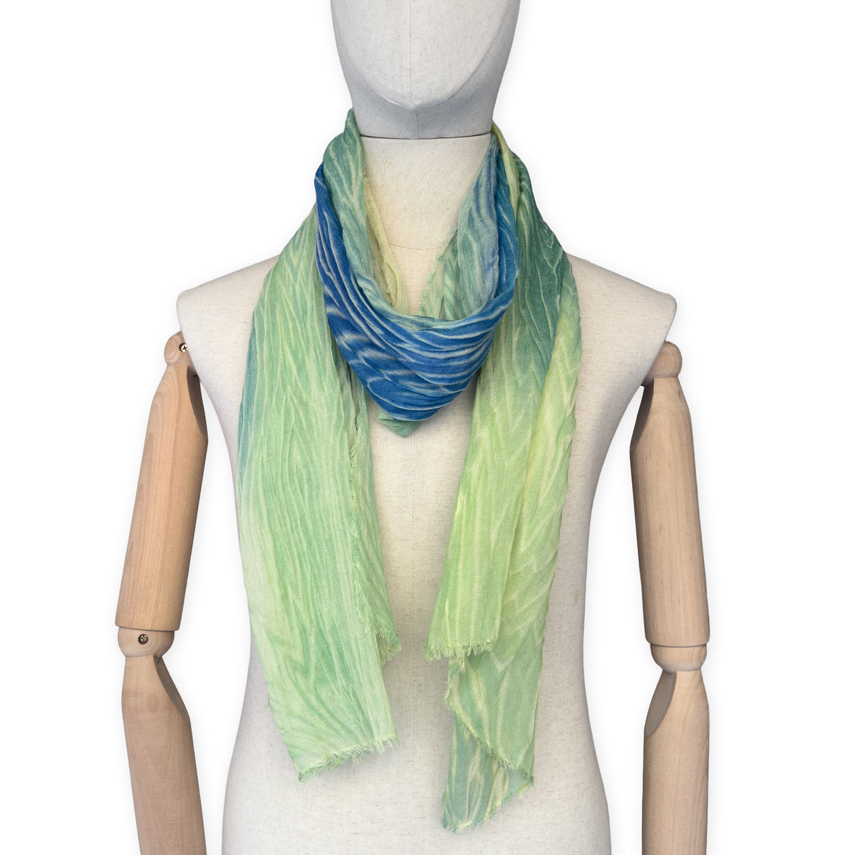 Mannequin wearing scarf on a white background. Hand-painted mix wool and silk scarf by Otta-Italy, 193 x 54 cm, featuring blue, light green and yellow colors. Luxury Italian accessory, soft and warm scarf for women and men.
