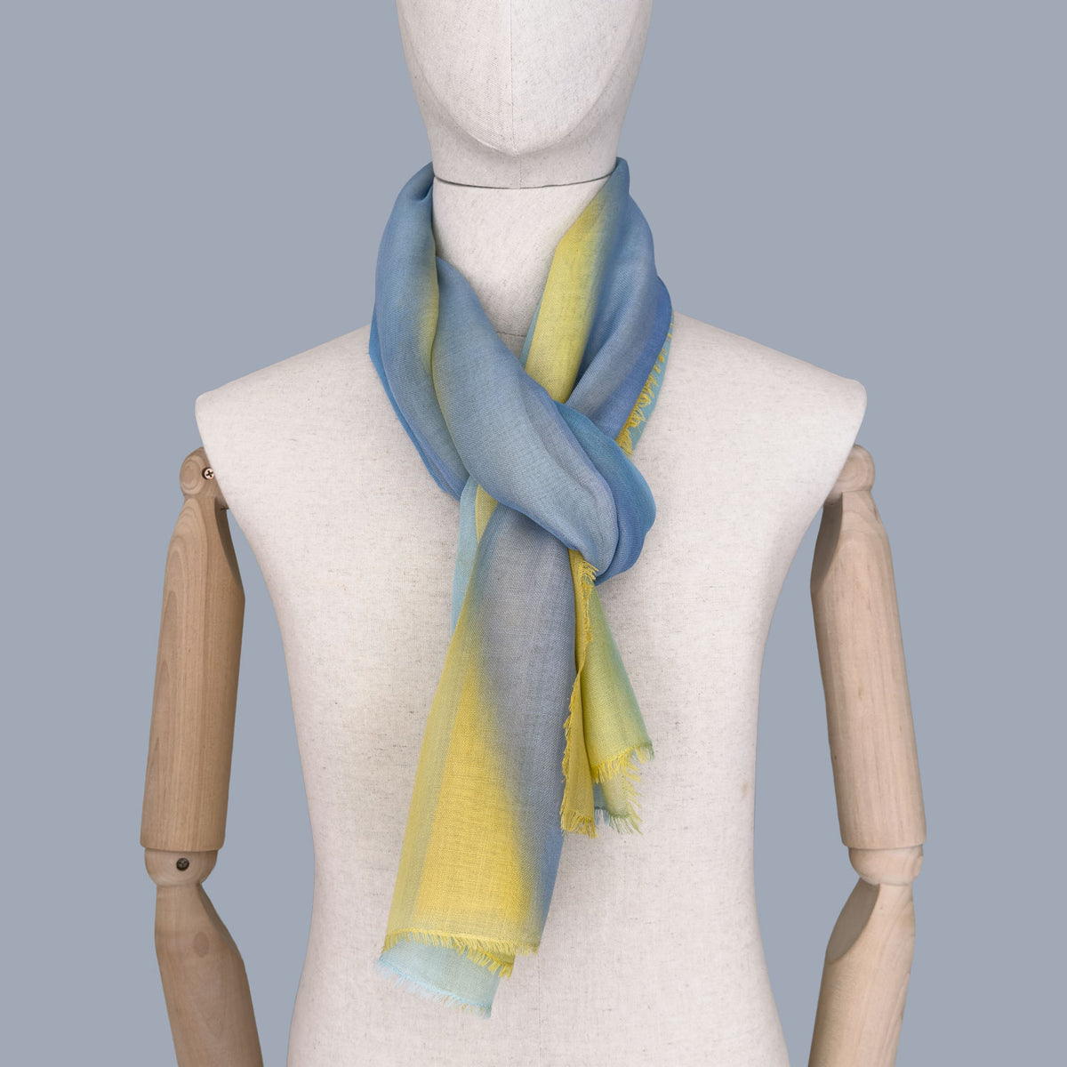 Mannequin wearing a hand-painted wool silk blend scarf by Otta-Italy, blue background. Blue and yellow shades. 70 x 198 cm.
