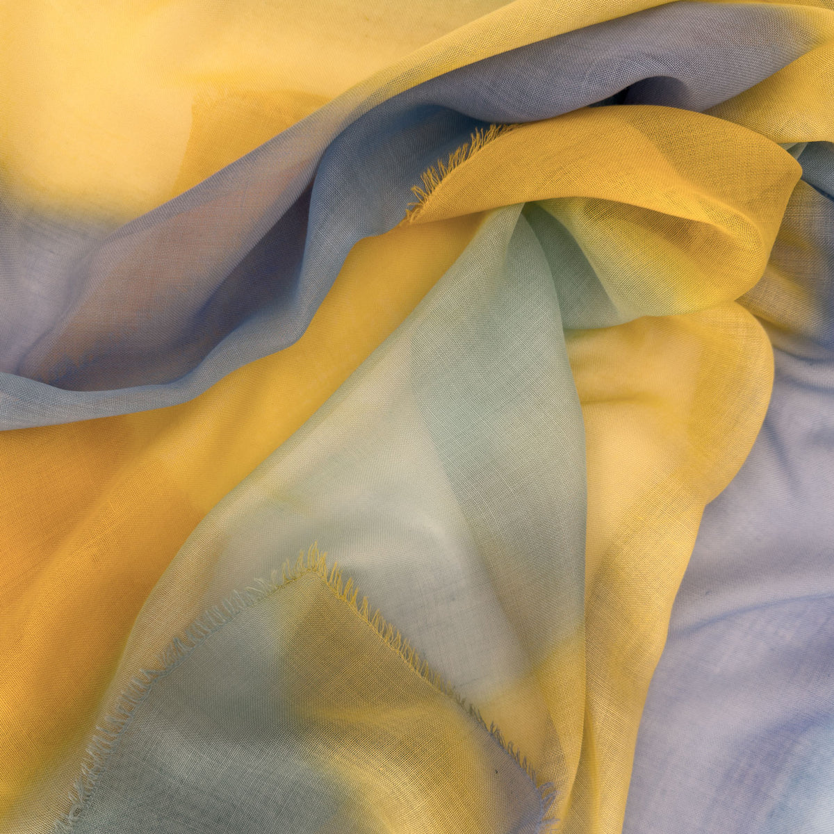 Close-up of hand-painted Otta wool silk blend scarf showcasing soft blue and yellow shades with delicate hand-fringed and hand-hemmed edges.
