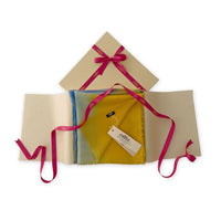 Luxury gift box with a pink ribbon containing a hand-painted Otta wool silk blend scarf on a white background.
