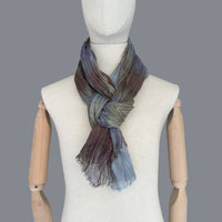 Mannequin wearing scarf on a gray background. Hand-painted wool & silk scarf by Otta-Italy, 54 x 193 cm, featuring 
light blue, purple, brown and green. Luxury Italian wool & silk accessory, soft and warm scarf for women and men.
