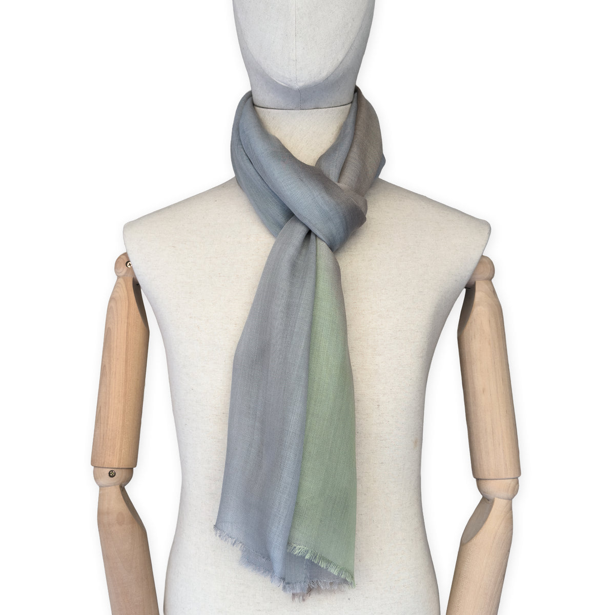 Mannequin wearing a hand-painted Otta wool & silk scarf on a white background in 
brown, gray and light green tones. Lightweight, warm, and elegant accessory measuring 70 x 197 cm. Unique artisan scarf with hand-fringed edges, perfect for women and men.
