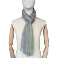 Mannequin wearing a hand-painted Otta wool & silk scarf on a white background in 
brown, gray and light green tones. Lightweight, warm, and elegant accessory measuring 70 x 197 cm. Unique artisan scarf with hand-fringed edges, perfect for women and men.
