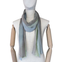 Mannequin wearing a hand-painted Otta wool & silk scarf on a white background in 
brown, gray and light green tones. Lightweight, warm, and elegant accessory measuring 70 x 197 cm. Unique artisan scarf with hand-fringed edges, perfect for women and men.
