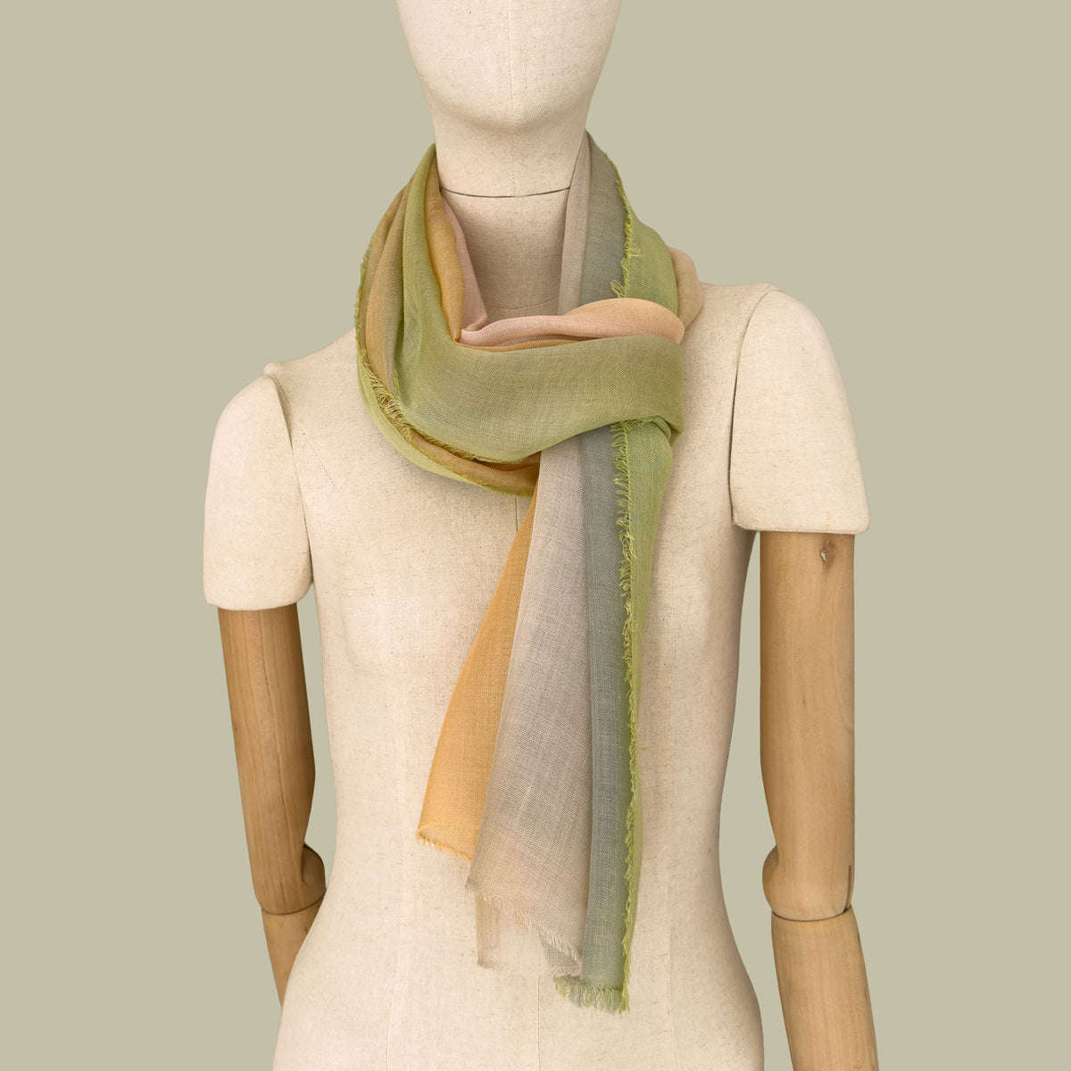 Mannequin wearing a hand-painted wool silk blend scarf by Otta-Italy, green background. Green, orange and beige shades. 71 x 199 cm.
