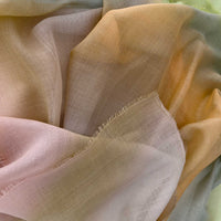 Close-up of hand-painted Otta wool silk blend scarf showcasing soft green, orange and beige shades with delicate hand-fringed and hand-hemmed edges.

