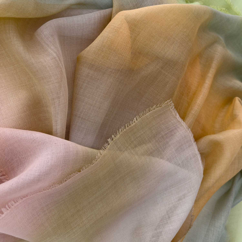 Close-up of hand-painted Otta wool silk blend scarf showcasing soft green, orange and beige shades with delicate hand-fringed and hand-hemmed edges.
