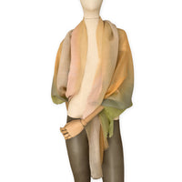 Mannequin wearing an elegant hand-painted Otta wool silk blend scarf on a white background. Warm green, orange and beige tones.
